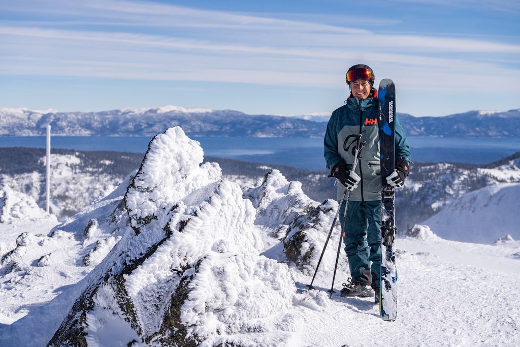 Picture of a man standing on a snowy ski mountain holding his skis and ski poles.